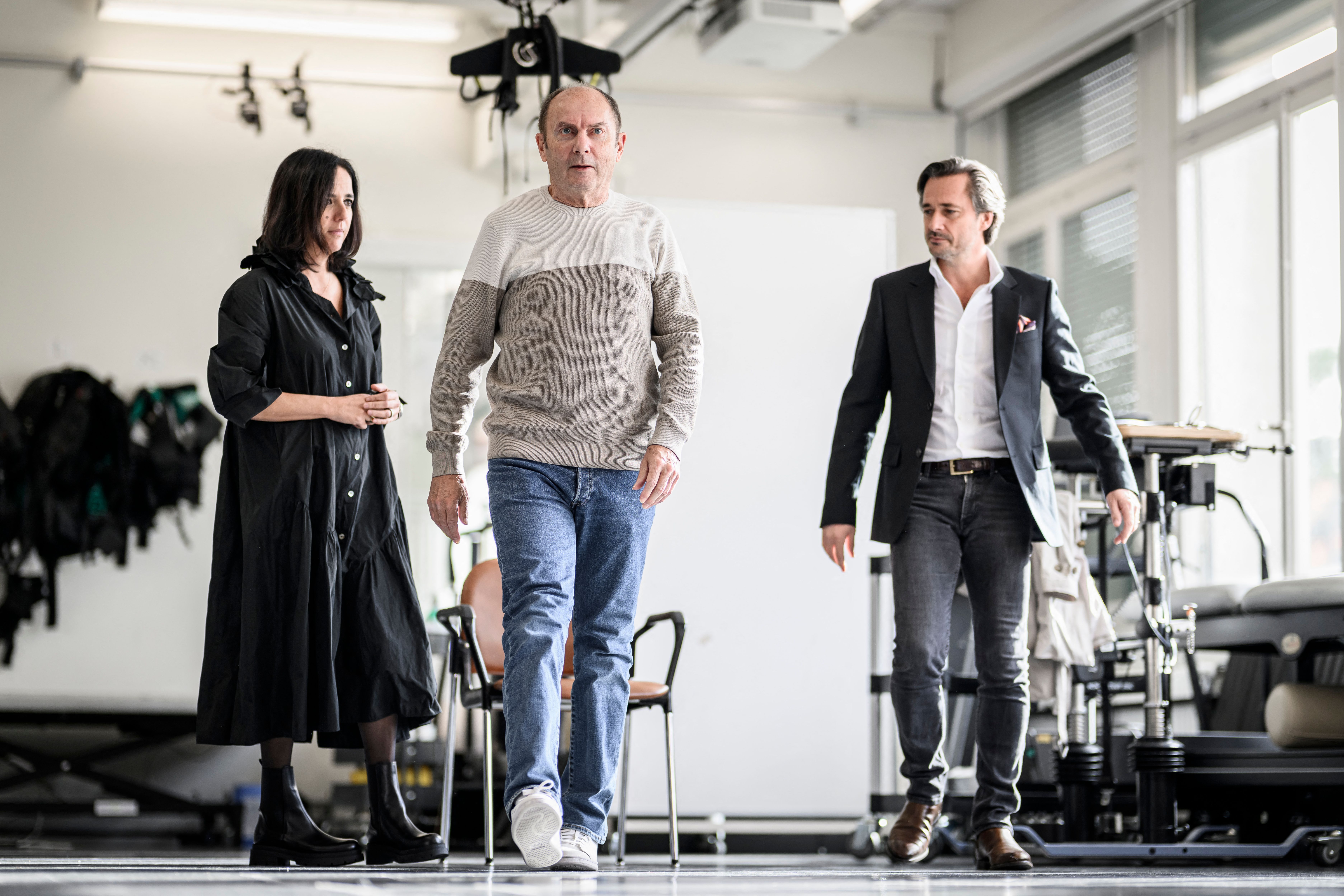 Swiss neurosurgeon, professor and co-director of NeuroRestore Jocelyne Bloch (L) and Swiss professor of neuroscience at the Swiss Federal Institute of Technology in Lausanne (EPFL) Lausanne University Hospital (CHUV) and Lausanne University (UNIL) and co-director of NeuroRestore, Gregoire Courtine (R), walk with Marc (C) a French patient suffering from Parkinson's disease fitted with a new neuroprosthesis during the presentation of a new neuroprosthesis that restores fluid walking in Lausanne, on November 3, 2023. Neuroscientists from Inserm, CNRS and the University of Bordeaux in France, together with Swiss researchers and neurosurgeons (EPFL/CHUV/UNIL), have designed and tested a 'neuroprosthesis' designed to correct the walking problems associated with Parkinson's disease. (Photo by GABRIEL MONNET / AFP) /